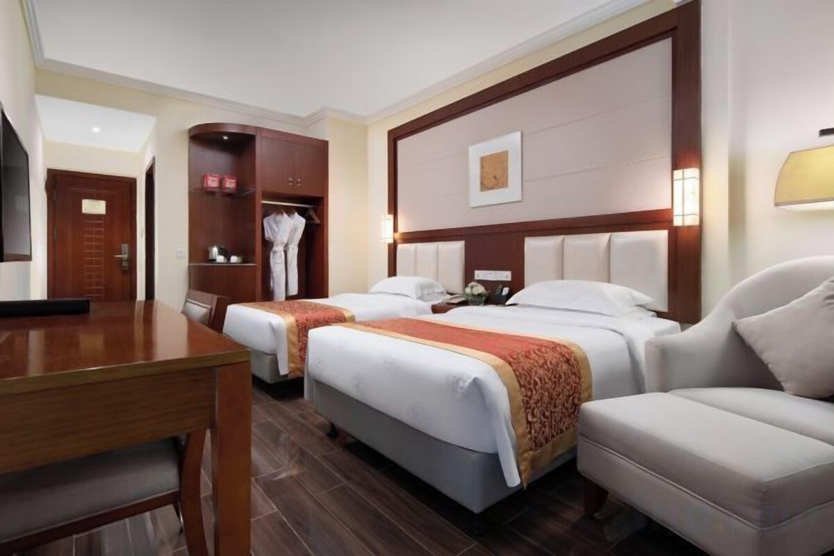 A hotel room with two beds, a desk, a wardrobe, and a sofa.