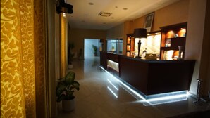 Un'area reception di un hotel con una scrivania, una pianta in vaso e un corridoio che porta a un'altra stanza.