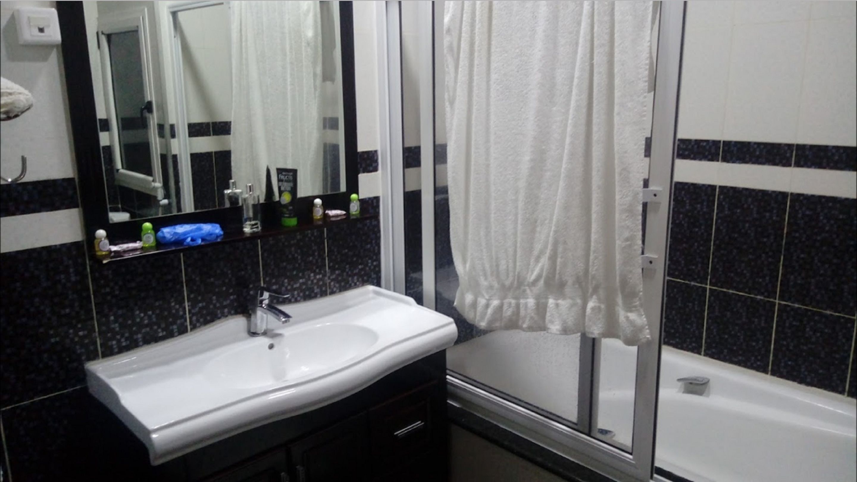 A bathroom with a white sink, a mirror, a shower with a white curtain, and dark tiled walls.