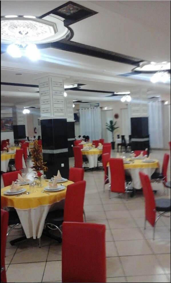 Un comedor con mesas redondas cubiertas con manteles amarillos y sillas rojas.