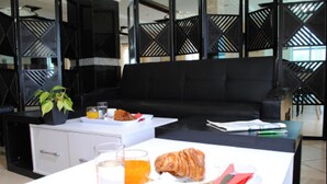 Un soggiorno moderno con un divano nero, un tavolo da pranzo con cose per la colazione e una pianta in vaso.