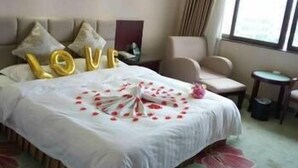 A hotel room with a large bed, a headboard, a small table, a chair, and a window with curtains. - Guifeng Hotel (Jiangmen)