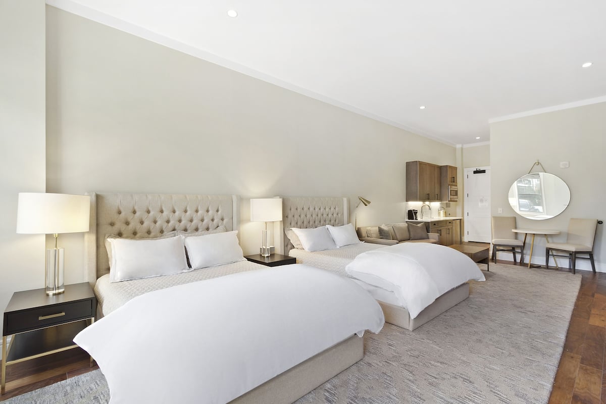 A hotel room with two large beds, a sitting area with a round table, and a mirror on the wall.