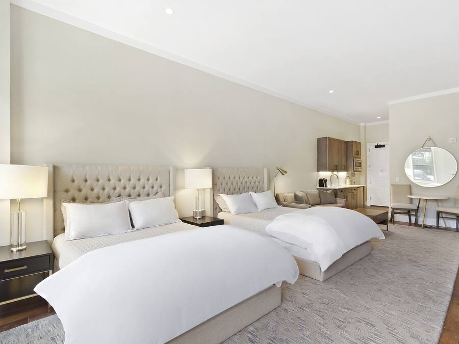 Quarto de hotel com duas camas grandes, área de estar com uma mesa redonda e espelho na parede.