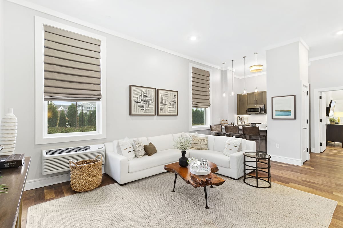 A modern living room with a white sofa, a coffee table, and a kitchen in the background.