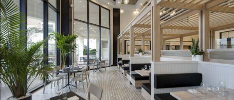 A modern restaurant with high ceilings, large windows, and a herringbone floor pattern.