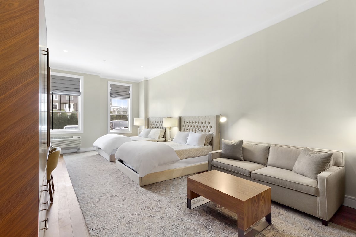 A modern hotel room with a large bed, a sofa, a coffee table, and a TV.