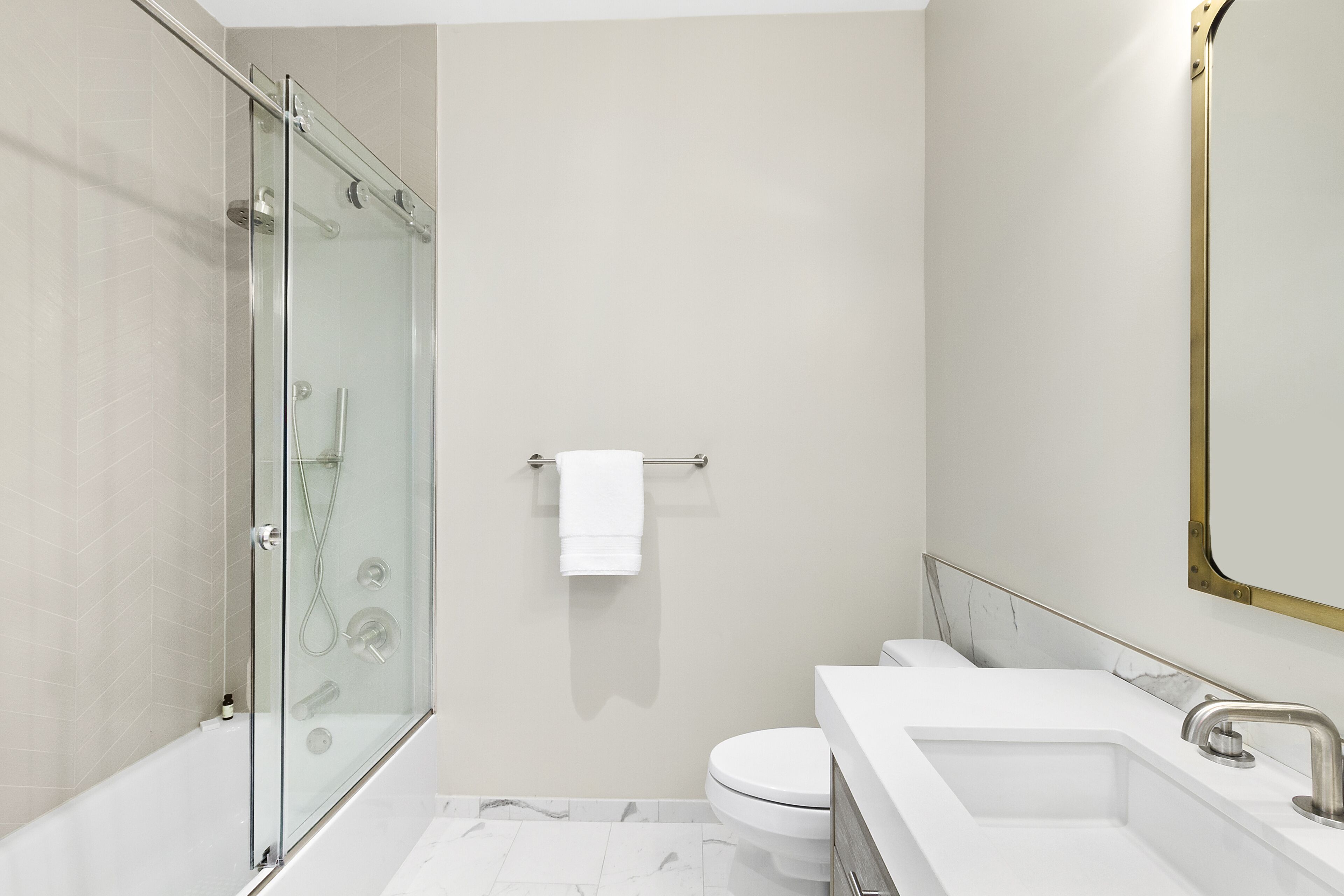 A modern bathroom with a glass-enclosed shower, a white toilet, and a sink with a gold faucet.