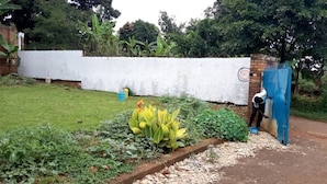 Un jardín con un muro blanco, una verja azul y una persona trabajando cerca de la verja.