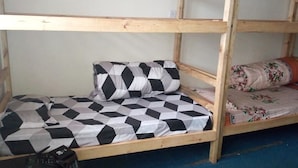 Una cama litera con colchón y almohadas de estampado geométrico, estructura de madera y suelo cubierto de moqueta azul.