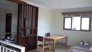 Una habitación con una mesa de comedor de madera, una silla, una cama con manta a rayas, una ventana con persianas y una estantería de madera.