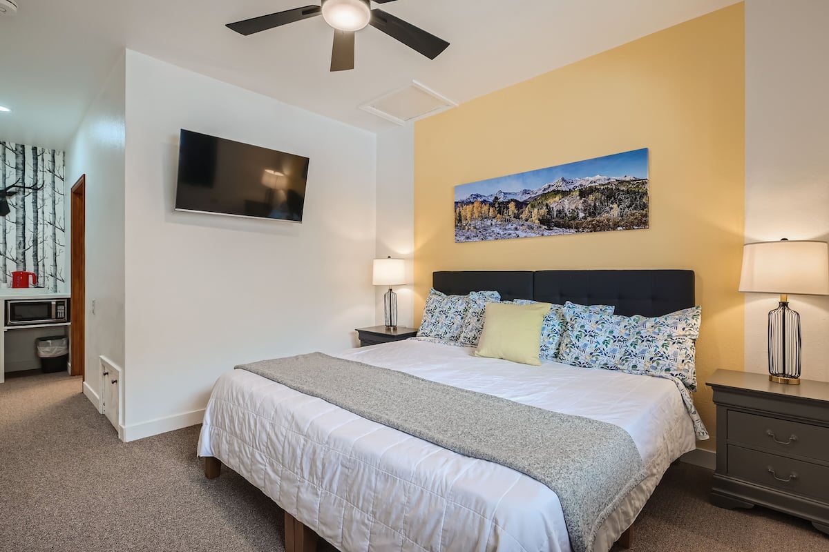 Ein Schlafzimmer mit Bett, Nachttischen, Deckenventilator, Fernseher und einem Bild an der Wand.