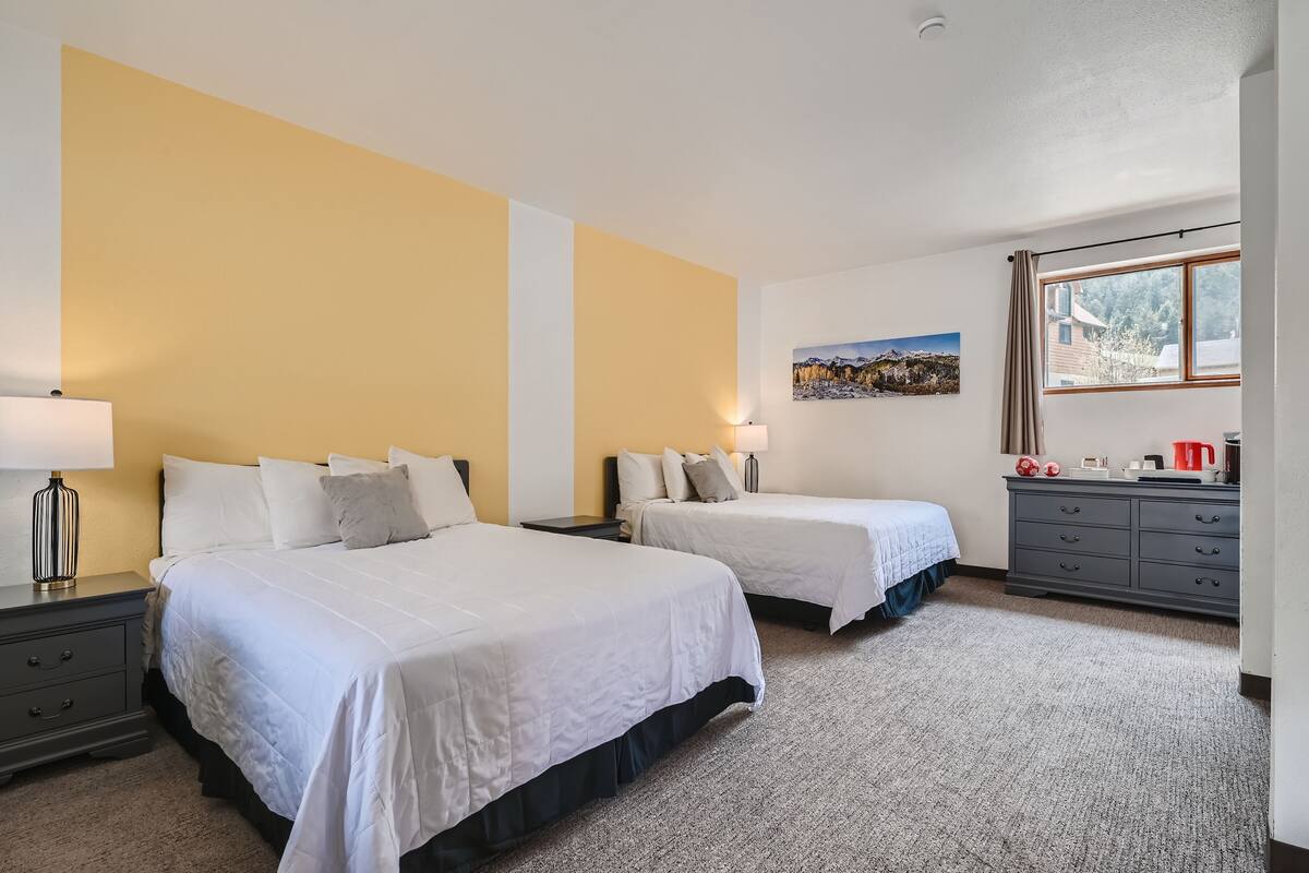 Ein Hotelzimmer mit zwei Betten, einer grauen Kommode, einem Bild an der Wand und einem Fenster mit Blick.