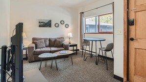 A living room with a sofa, coffee table, TV, and a dining area with chairs and a table. - Uplift Inn (Idaho Springs)