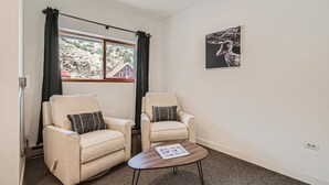 A room with two beige armchairs, a small wooden table, a black and white artwork on the wall, and a window with black curtains. - Uplift Inn (Idaho Springs)