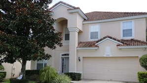 Une maison à deux étages, avec une façade de couleur beige, un toit en tuiles et un garage.