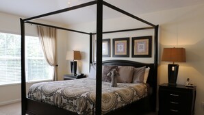 Un lit à baldaquin avec une couvre-lit à motifs, deux tables de chevet avec des lampes et des tableaux encadrés accrochés au mur.