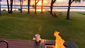 A deck with a grill and a cup, overlooking a grassy area with trees and a body of water.