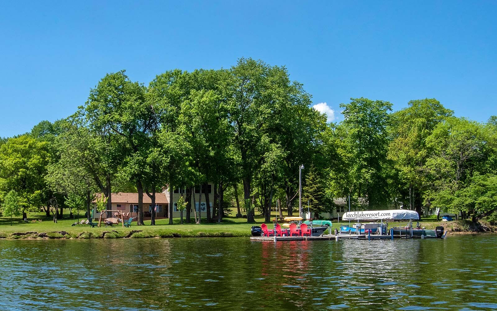Un parque junto al lago con un muelle para barcos, mesas de picnic y un edificio al fondo.
