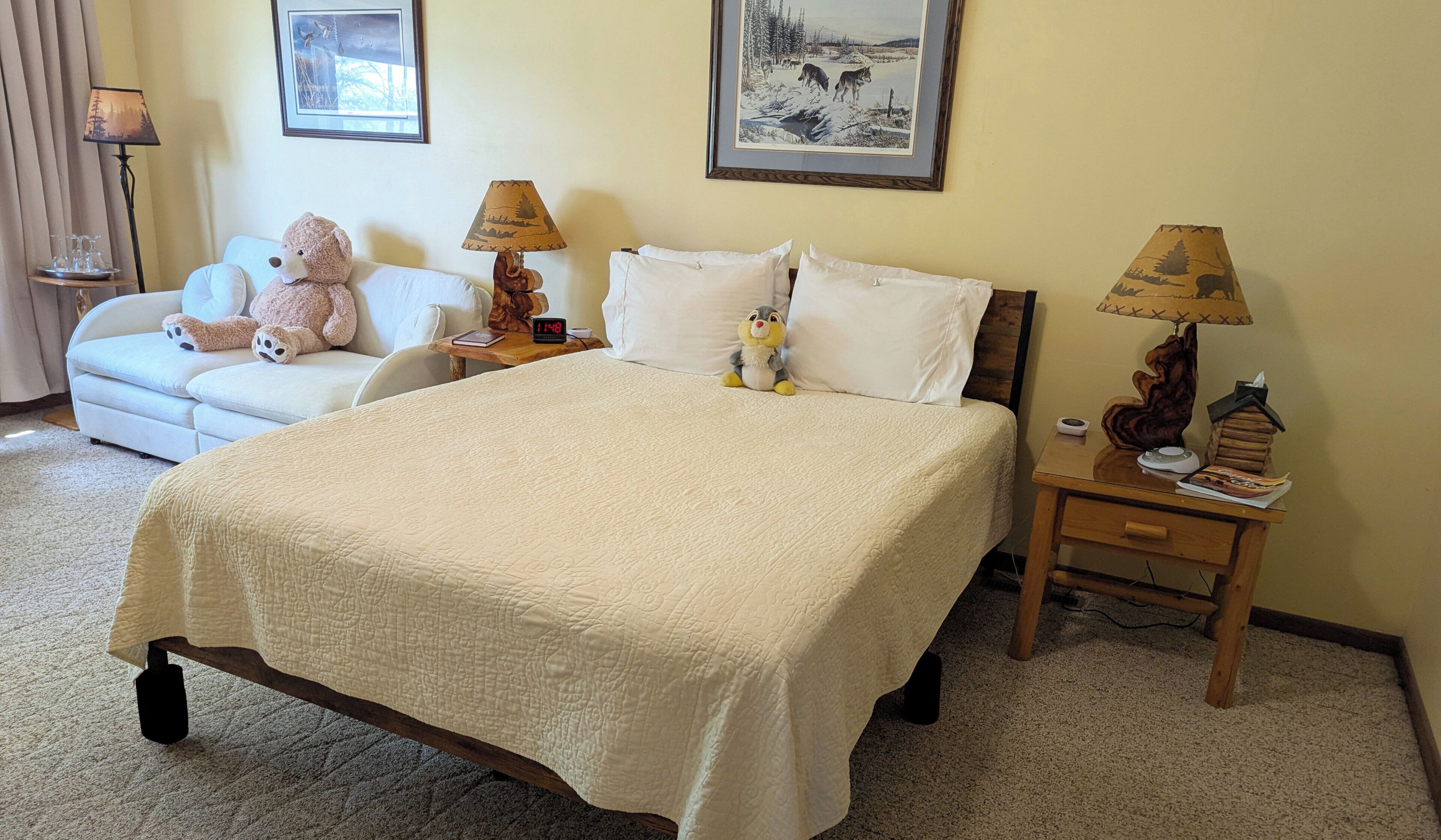 A neatly arranged hotel room with a large bed, a sofa, two lamps, and a framed picture on the wall.
