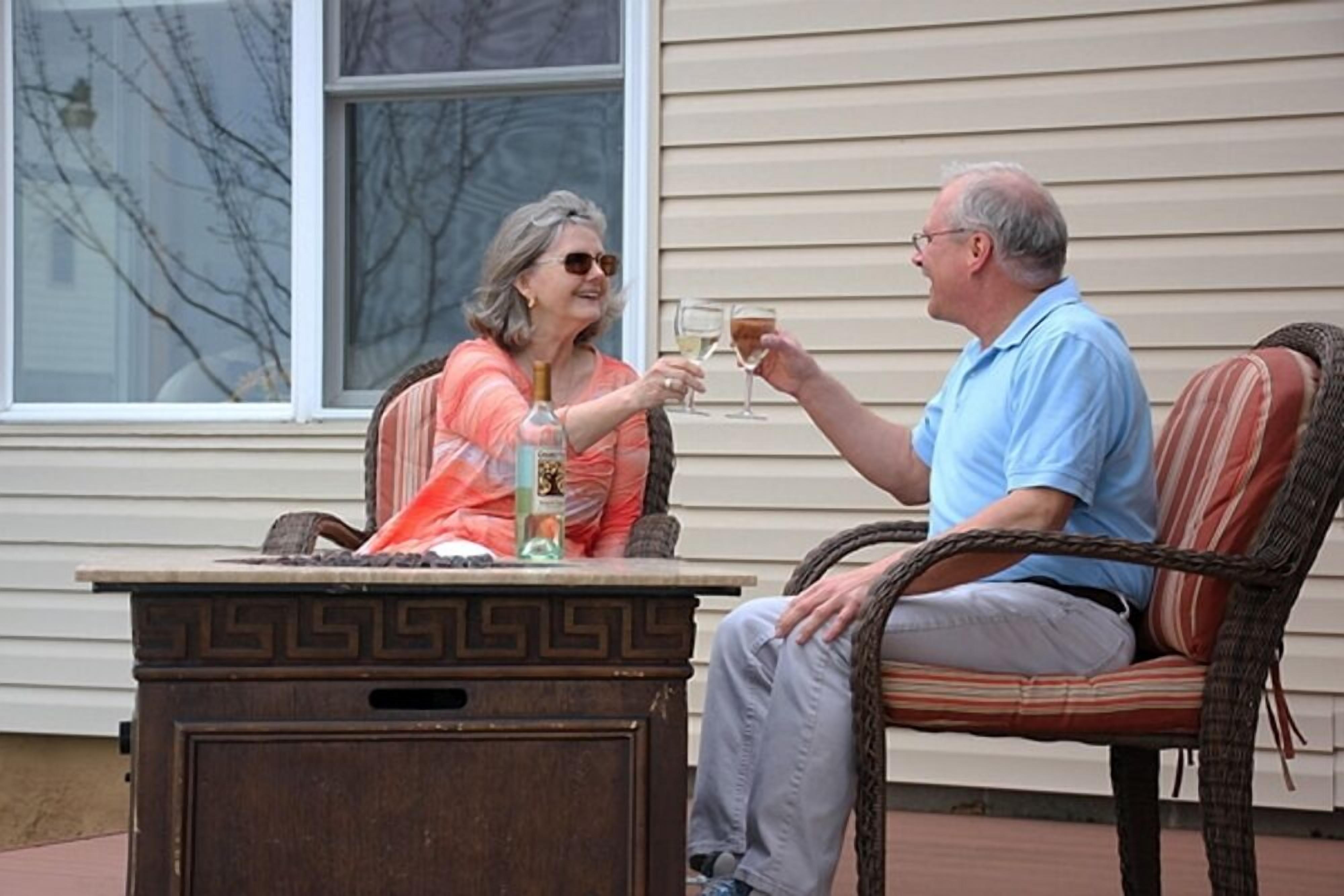 Two people seated at an outdoor table with drinks, a wicker chair, and a decorative table base.