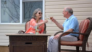 Two people seated at an outdoor table with drinks, a wicker chair, and a decorative table base.
