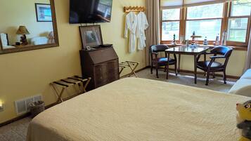 A hotel room with a bed, a desk, two chairs, a television, and a window with a view.
