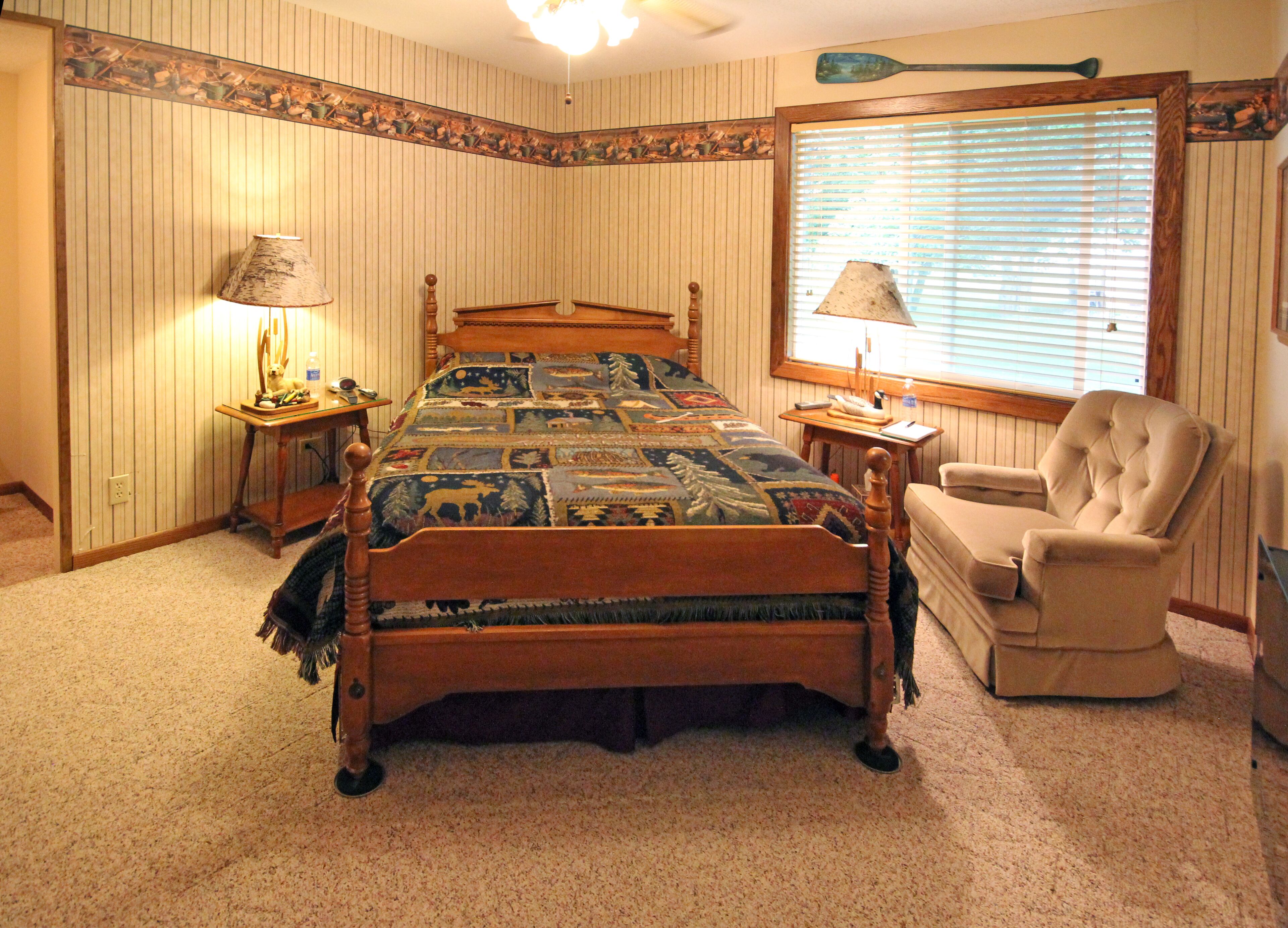 Een slaapkamer met een houten bed, twee nachtkastjes, een stoel en een raam met jaloezieën.