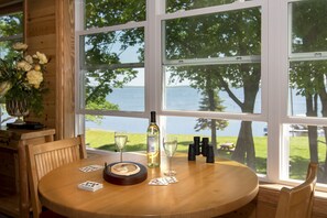 A wooden table with playing cards, a bottle of wine, and glasses, set against a window with a view of a lake and trees. - Leech Lake Resort Bed & Breakfast (Walker)