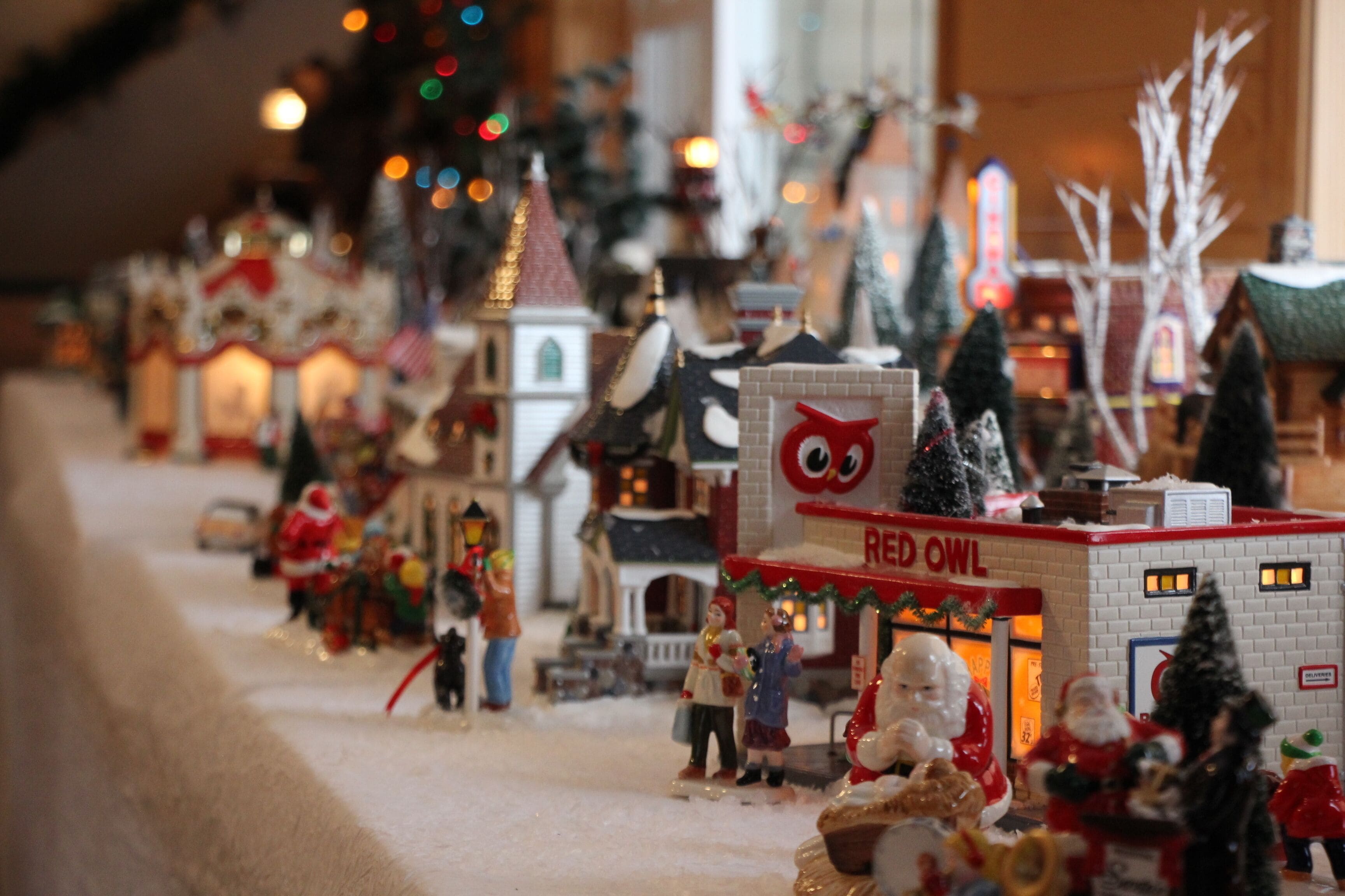 A miniature town model with various buildings, including a Red Owl store, and small figurines of people and Santa Claus.