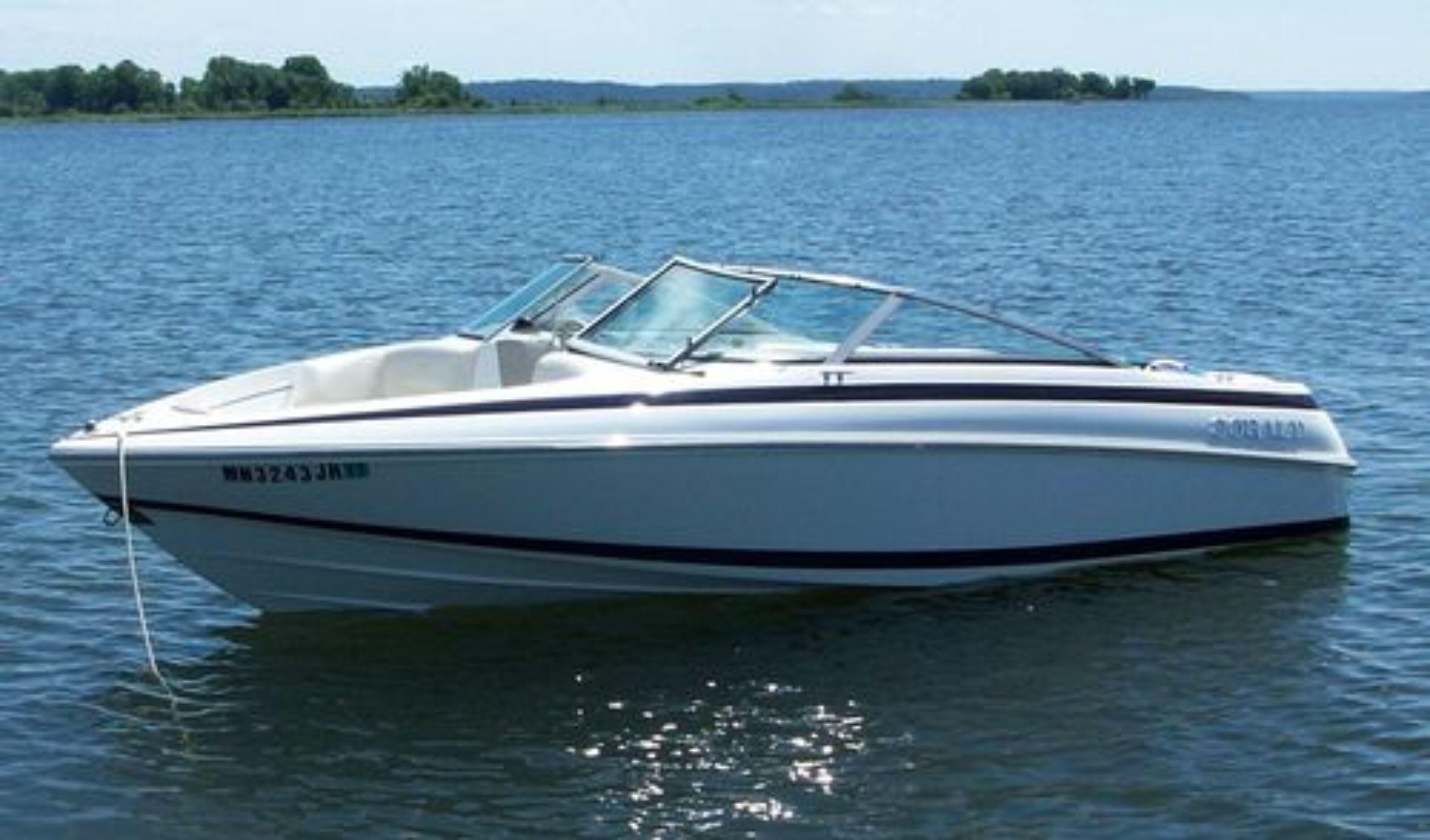 Un velero blanco con cabina, número de registro WM3243JH, en un lago tranquilo.
