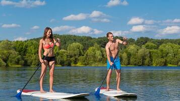 Two people paddleboarding on a calm lake with a forested shoreline in the background.