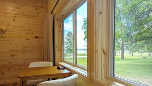 A wooden cabin with a dining table and chairs, large windows offering a view of a grassy area and trees.