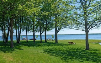 Un parque junto al lago con árboles, un bote y una hamaca.