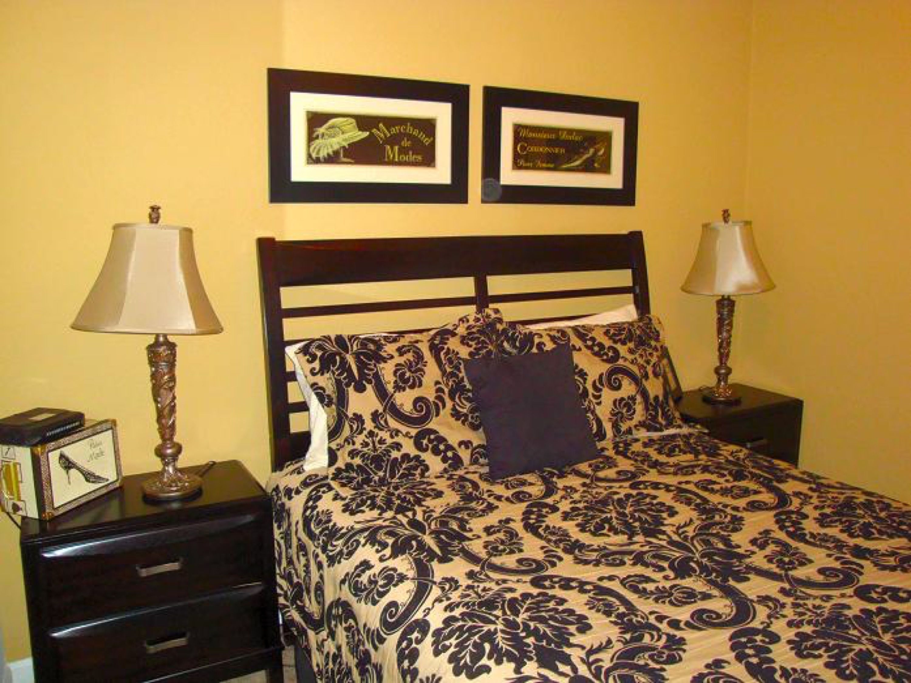 A bedroom with a bed, two nightstands, two lamps, and two framed certificates on the wall.