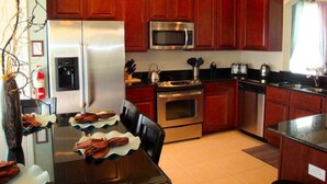 A modern kitchen with wooden cabinets, stainless steel appliances, and a dining area with a table set for two. - 6BR 4BA Home in Windsor Hills by CV-2564 (Kissimmee)