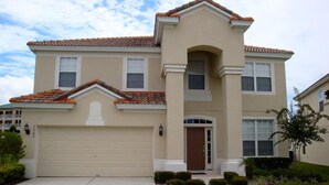 A two-story house with a beige facade, a brown front door, and a tiled roof. - 6BR 4BA Home in Windsor Hills by CV-2564 (Kissimmee)