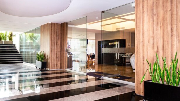 Een moderne hotellobby met een glazen wand, een houten receptiebalie en een trap naar een andere verdieping.