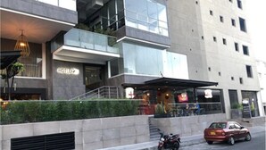 Een modern hotel met een glazen gevel, een zichtbaar restaurant, en een geparkeerde auto en motorfiets op de straat.