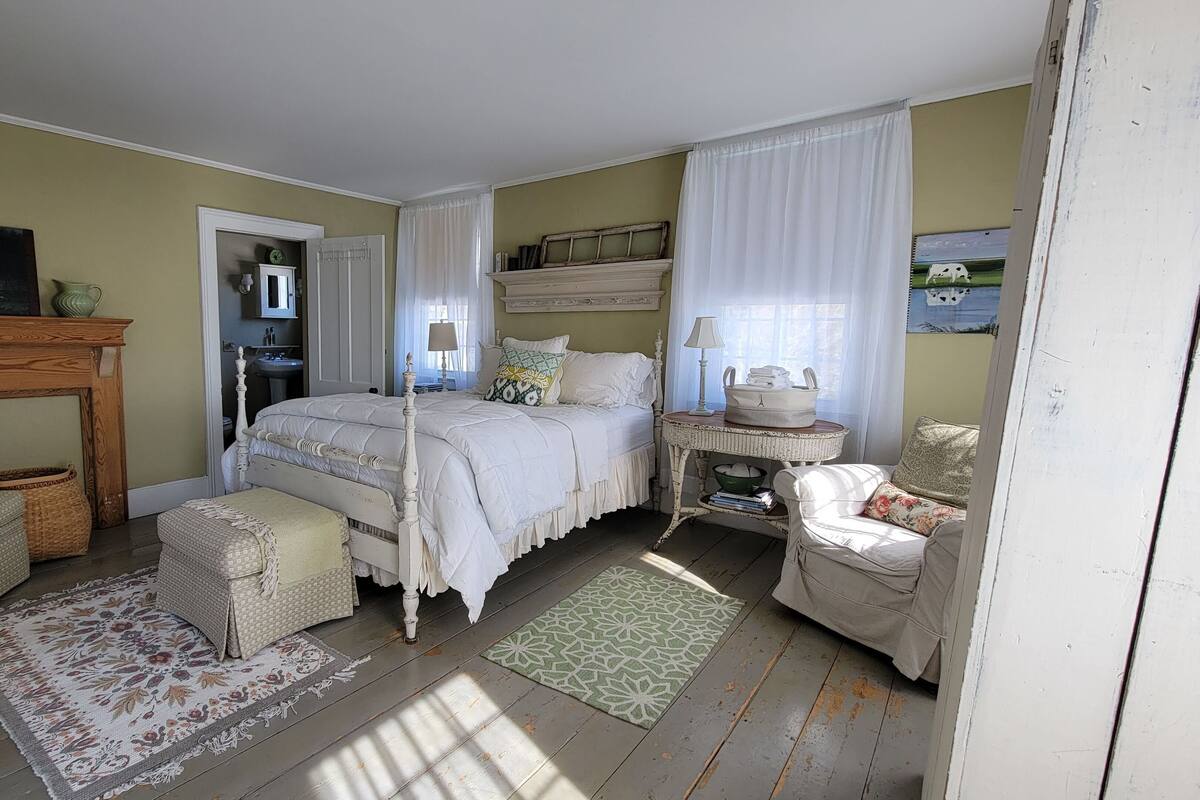 Une chambre à coucher avec un lit en bois, une cheminée, une petite table avec une lampe et une chaise.