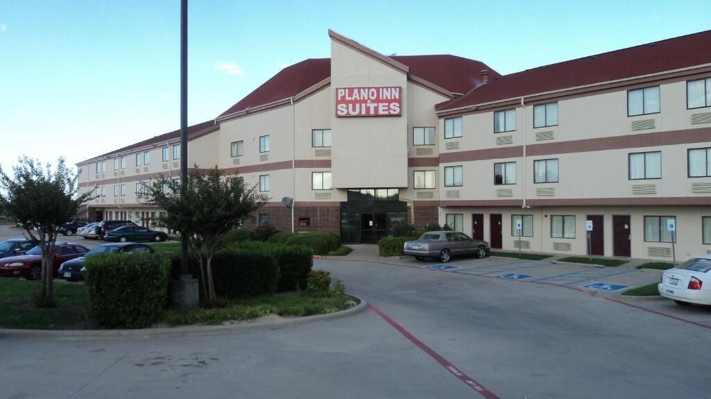 Un hotel amb un rètol que diu "PLANO INN SUITES" i diverses places d'aparcament, inclosos espais reservats per a persones amb discapacitat.