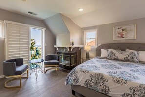 Quarto com cama grande, lareira, varanda com vista e duas poltronas.