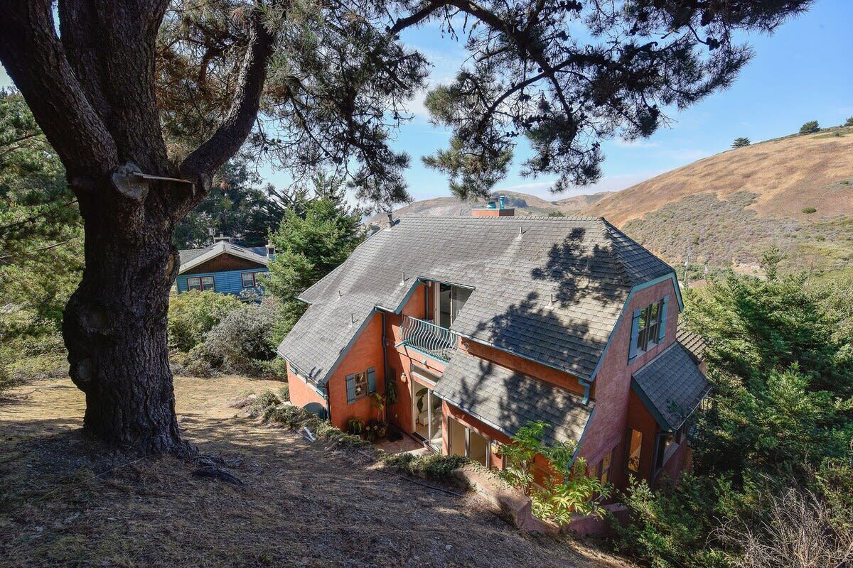 Una casa con techo inclinado, un balcón y un gran árbol en la parte delantera.