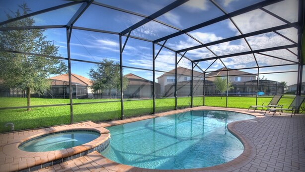 A covered swimming pool with a hot tub, surrounded by a brick patio and a metal fence. - 5BR 5BA Home in Windsor HIlls by CV-2622 (Kissimmee)