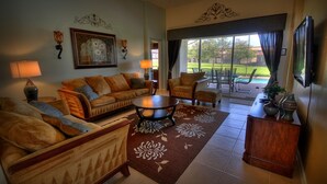 A living room with a sofa, armchairs, a coffee table, and a TV. There is a large window with a view of a lawn and a pool. - 5BR 5BA Home in Windsor HIlls by CV-2622 (Kissimmee)