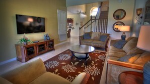 A living room with a flat-screen TV, a sofa set, a coffee table, and a patterned rug. - 5BR 5BA Home in Windsor HIlls by CV-2622 (Kissimmee)