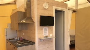 A compact kitchenette with a stove, sink, and a mounted TV. - Vento Etrusco - Camping (Piombino)