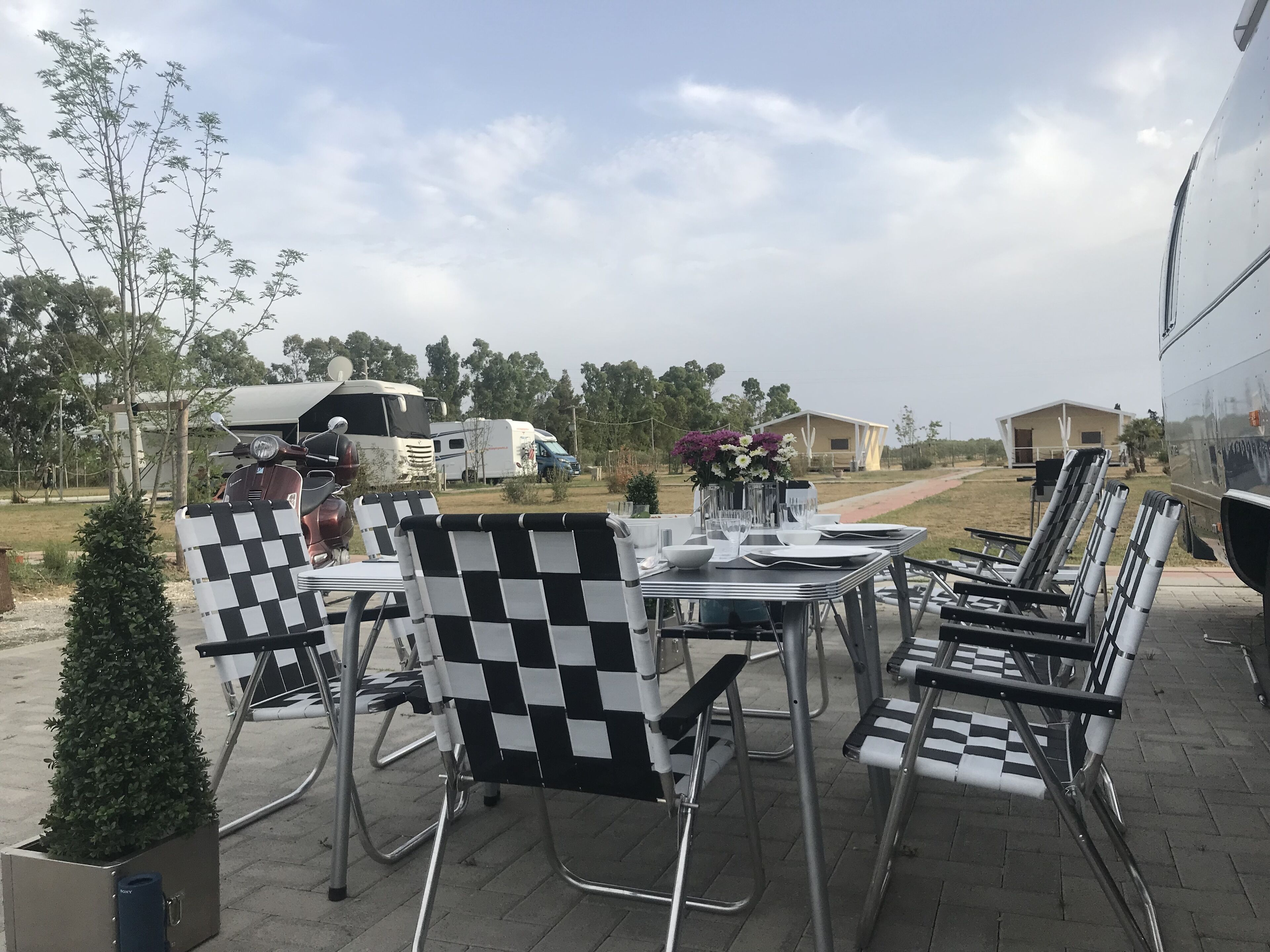 An outdoor seating area with checkered chairs and tables, a small potted plant, and a table with a vase of flowers.