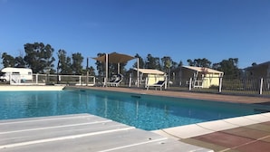 A swimming pool with sun loungers and a covered area, surrounded by a fence and trees. - Vento Etrusco - Camping (Piombino)