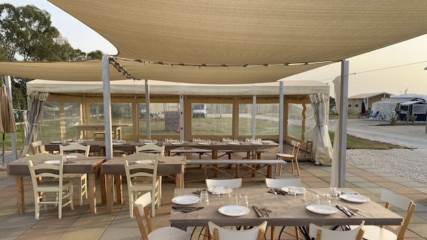 An outdoor dining area with multiple tables and chairs, covered by a large canopy. - Vento Etrusco - Camping (Piombino)